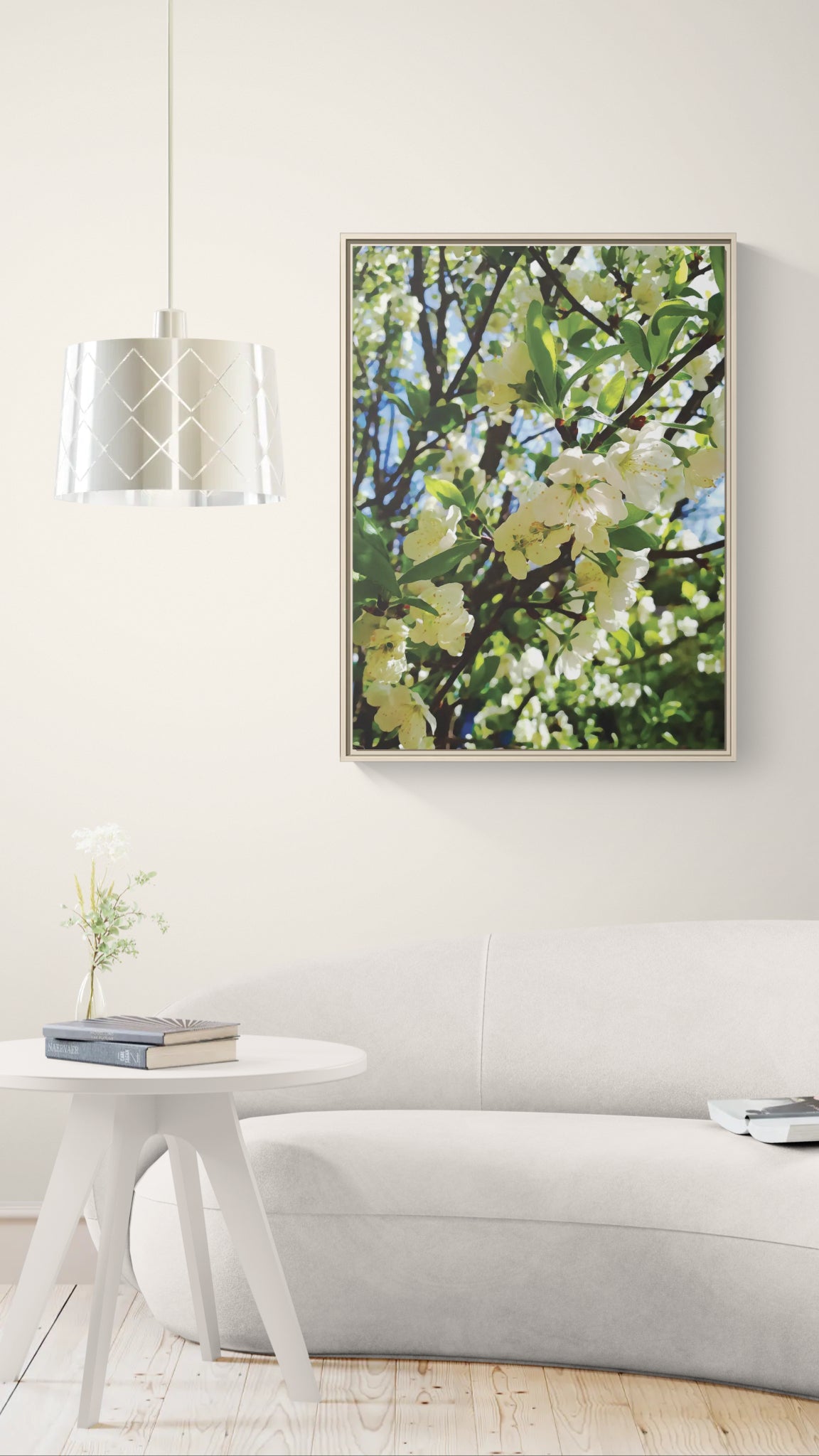 Framed wall art of white blossoms on a tree branch above a white sofa