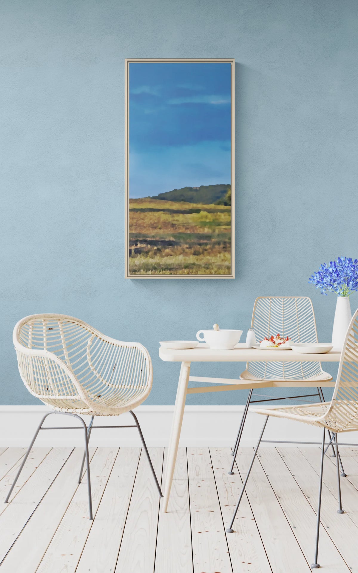 Vertical landscape canvas of a field and hills hanging on a blue wall above a dining table