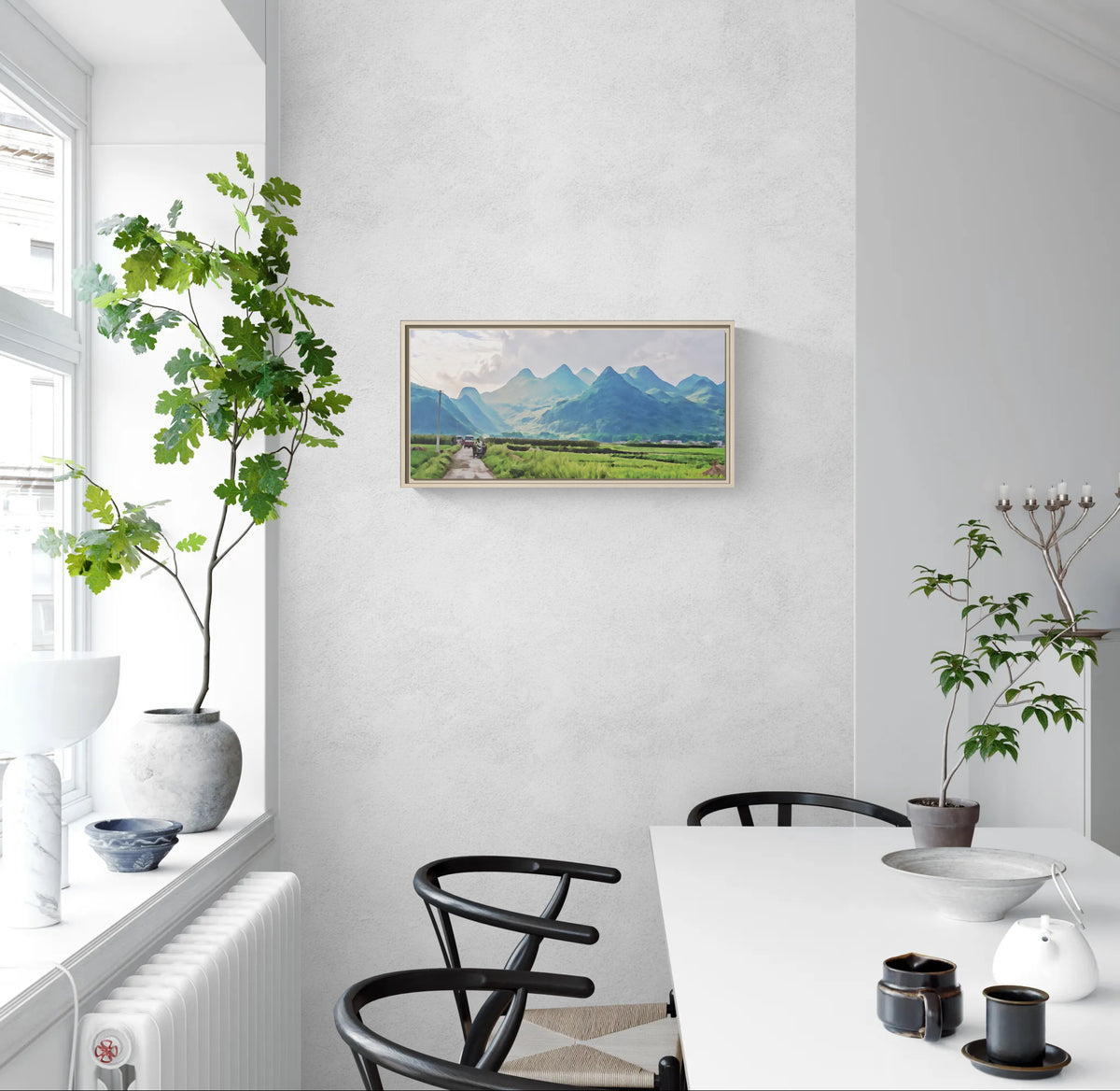 Framed landscape canvas of mountains and fields hanging on a white wall in a dining room