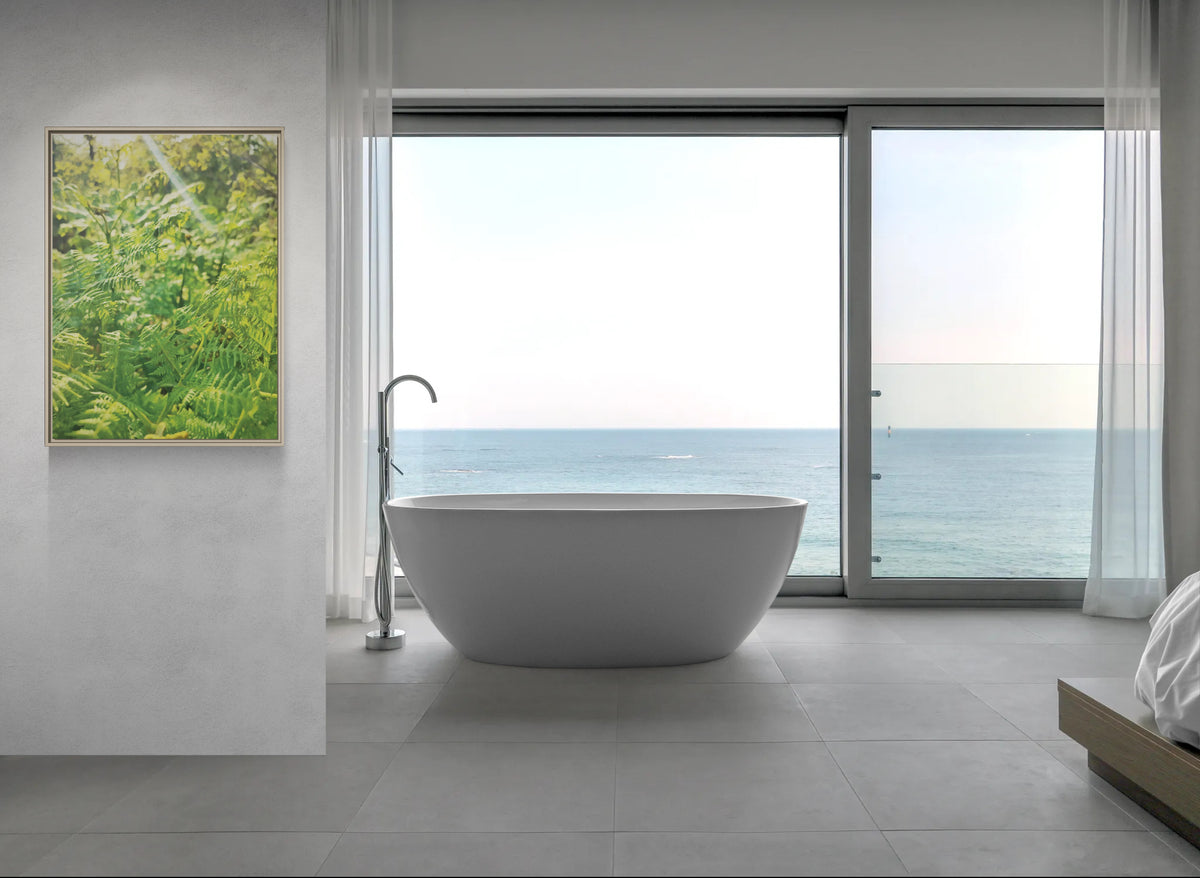 Freestanding white bathtub in front of a large window overlooking the ocean