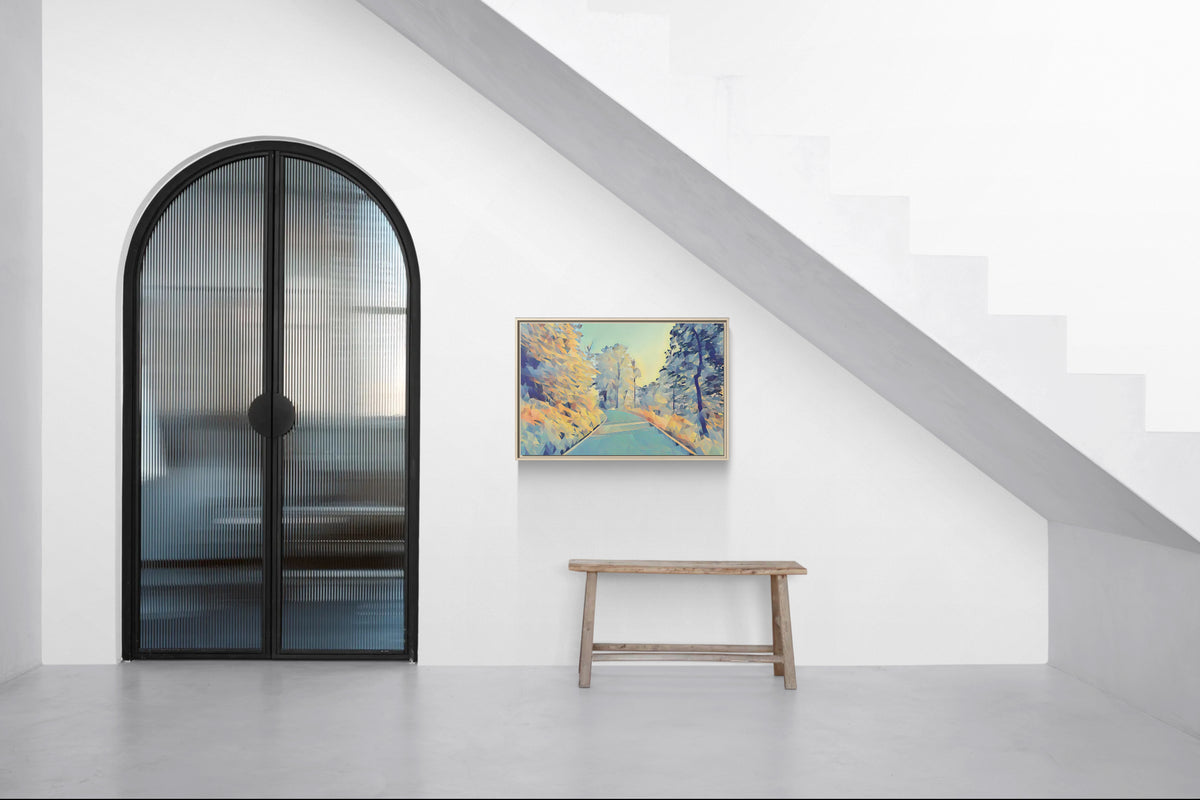 Framed landscape canvas hanging on a white wall next to an arched glass door and wooden bench