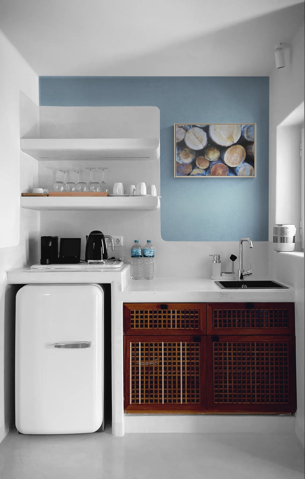 Kitchenette with white mini fridge, wooden lattice cabinets, open shelving, and blue accent wall with log print art