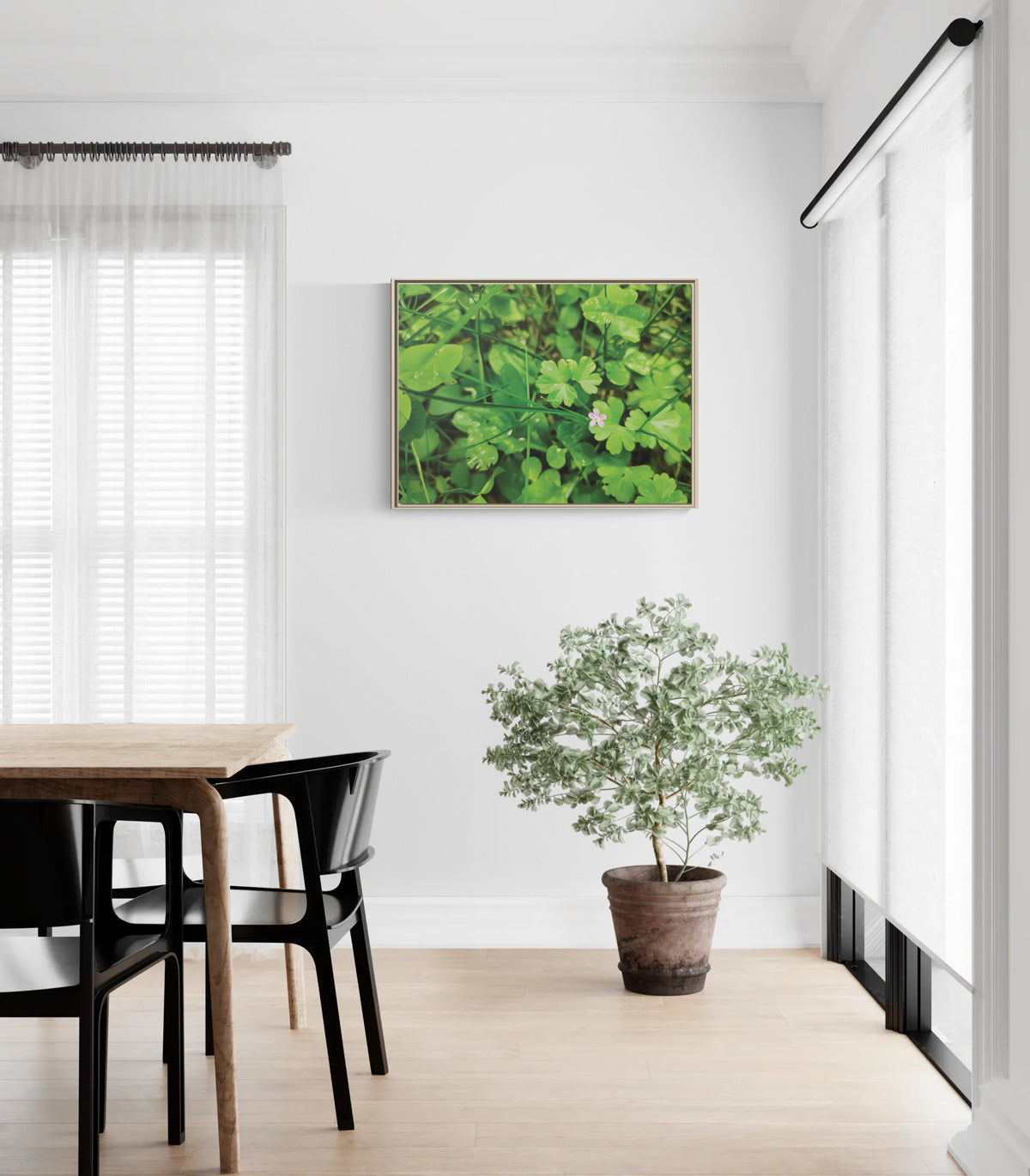 Framed nature print of green clover leaves with a small pink flower hanging on a white wall in a dining room