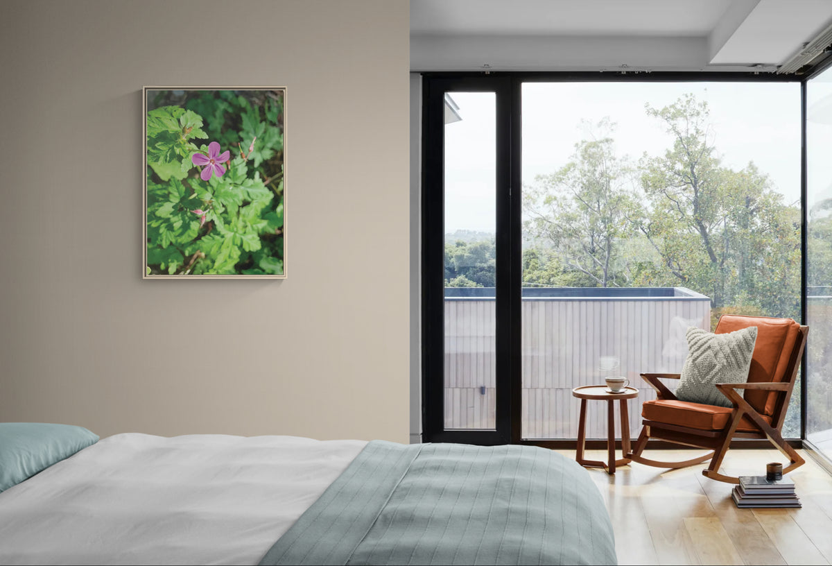 Framed botanical wall art featuring a pink flower hanging on a bedroom wall next to a rocking chair