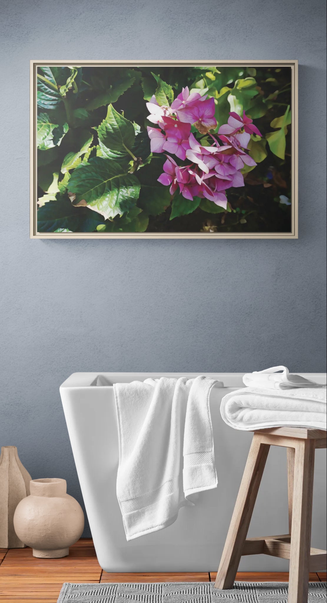 Framed floral wall art above a white bathtub with towels on a wooden stool