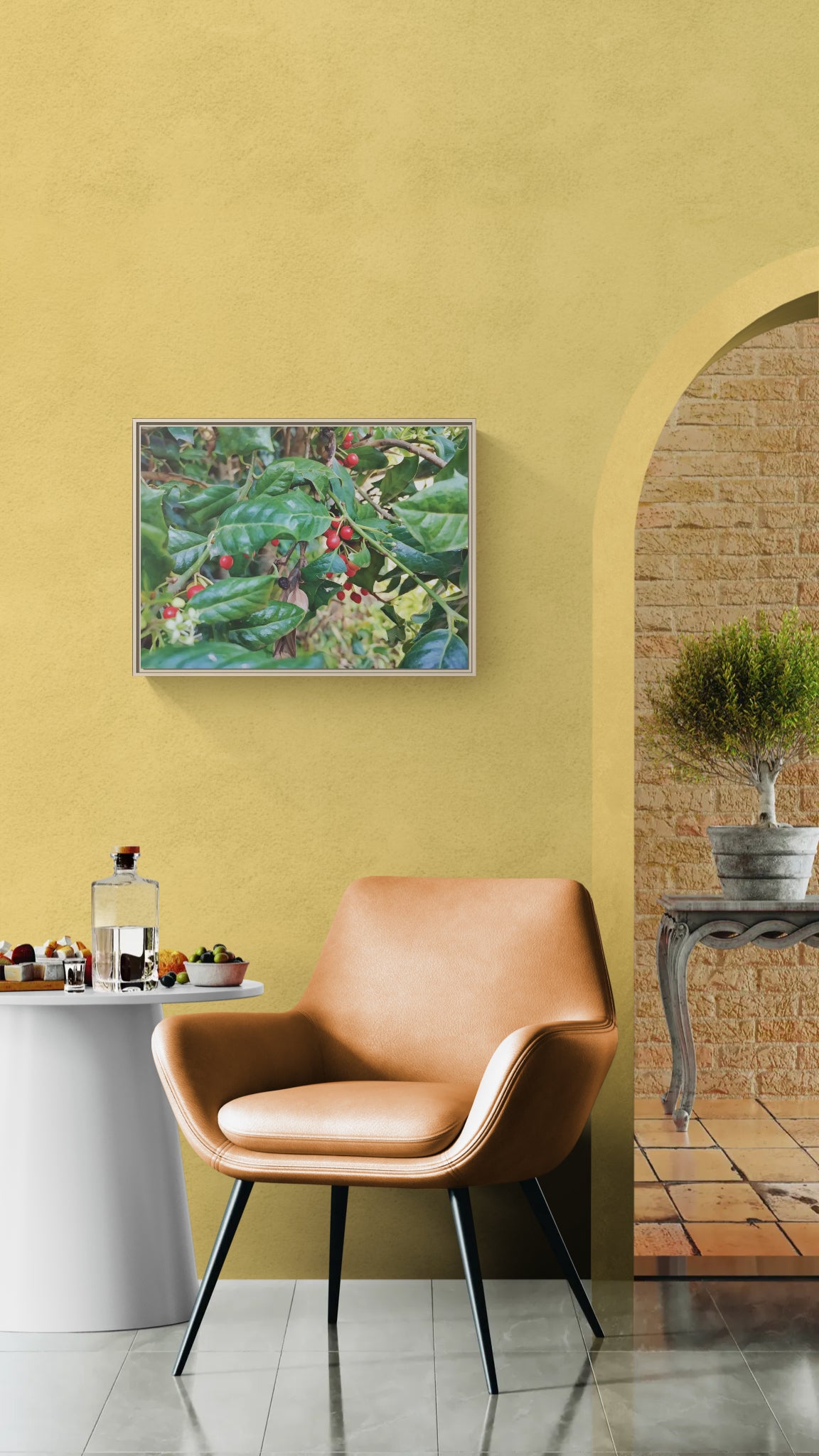 Framed wall art of coffee plant with red berries hanging on yellow wall above tan leather chair