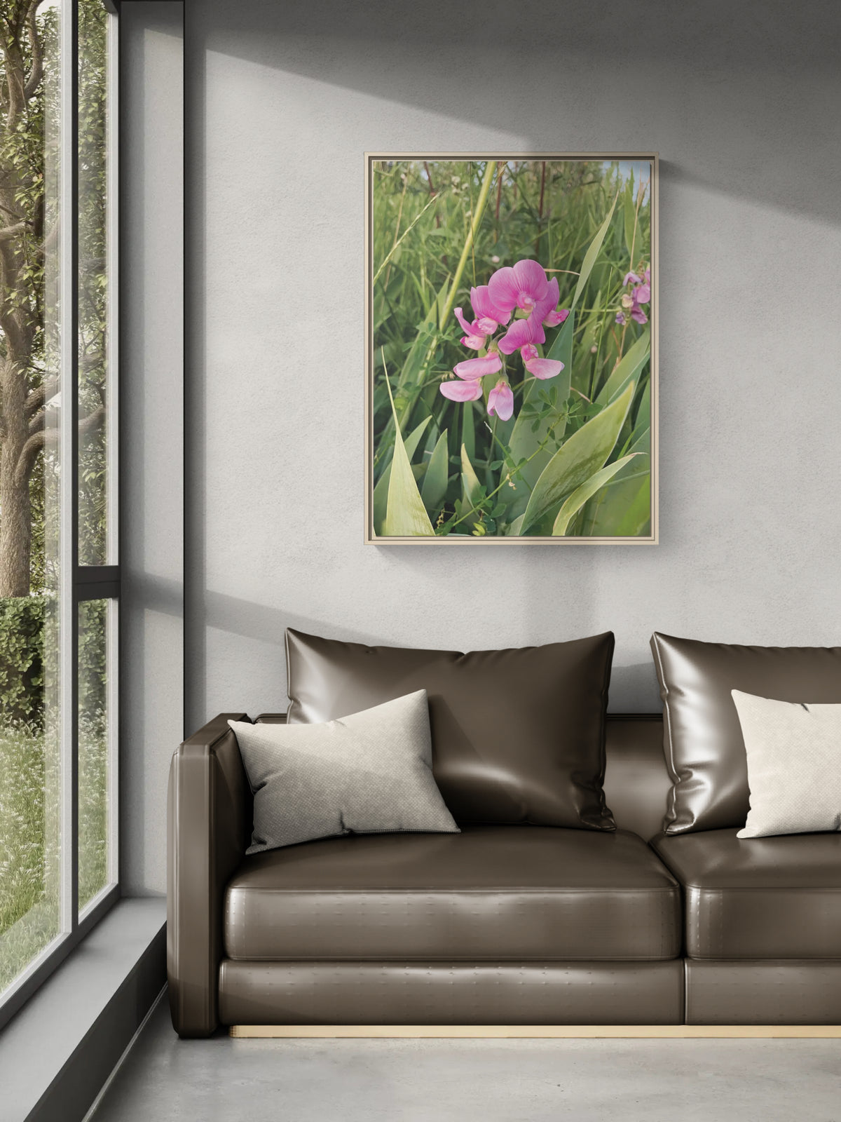 Framed wall art of pink wildflowers hanging above a brown leather sofa