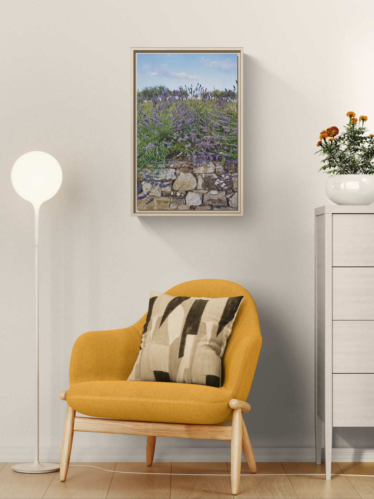Framed wall art of lavender growing over a stone wall hanging above a yellow armchair