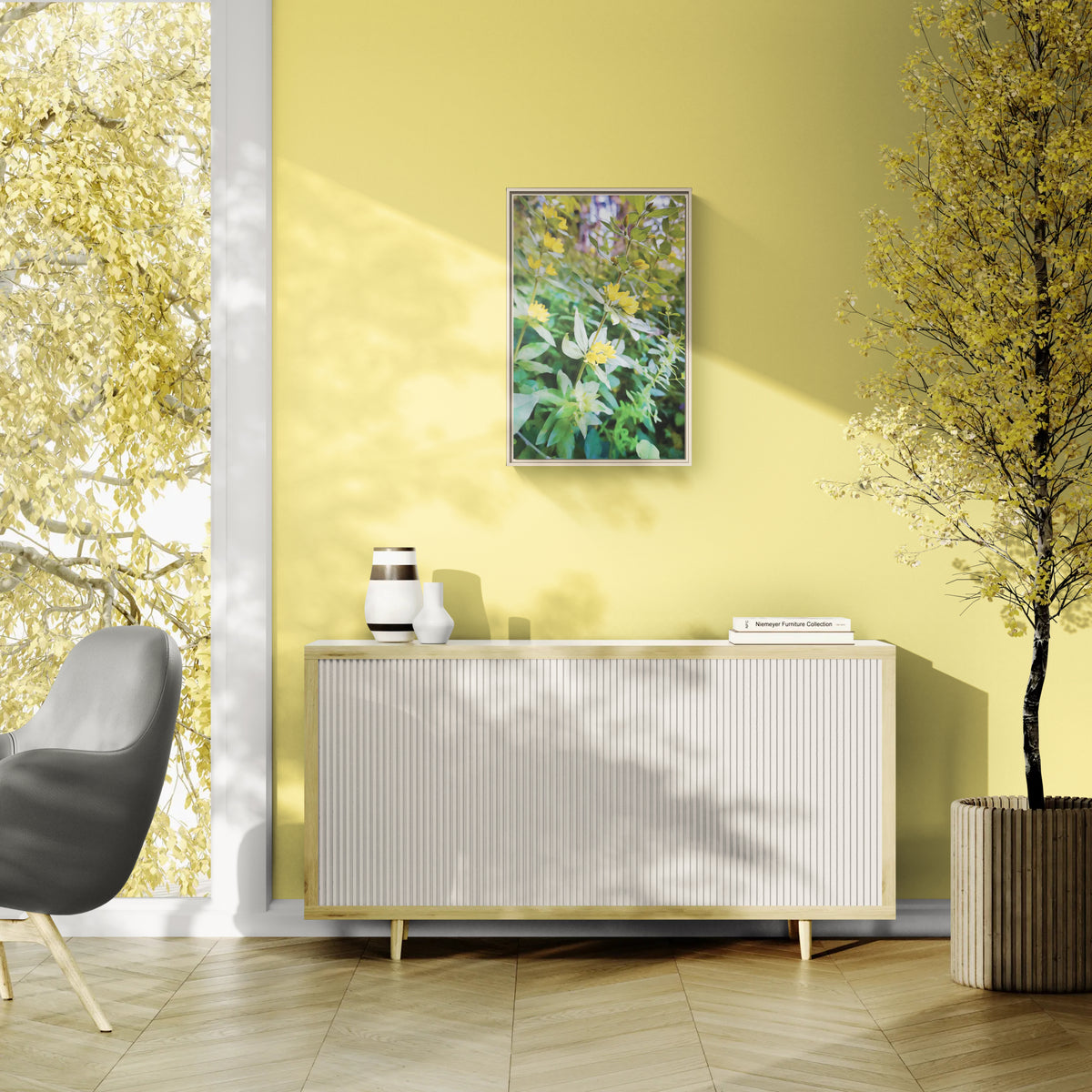 A framed floral art print hangs on a yellow wall above a white ribbed sideboard in a modern living room setting with a gray chair and a potted tree.