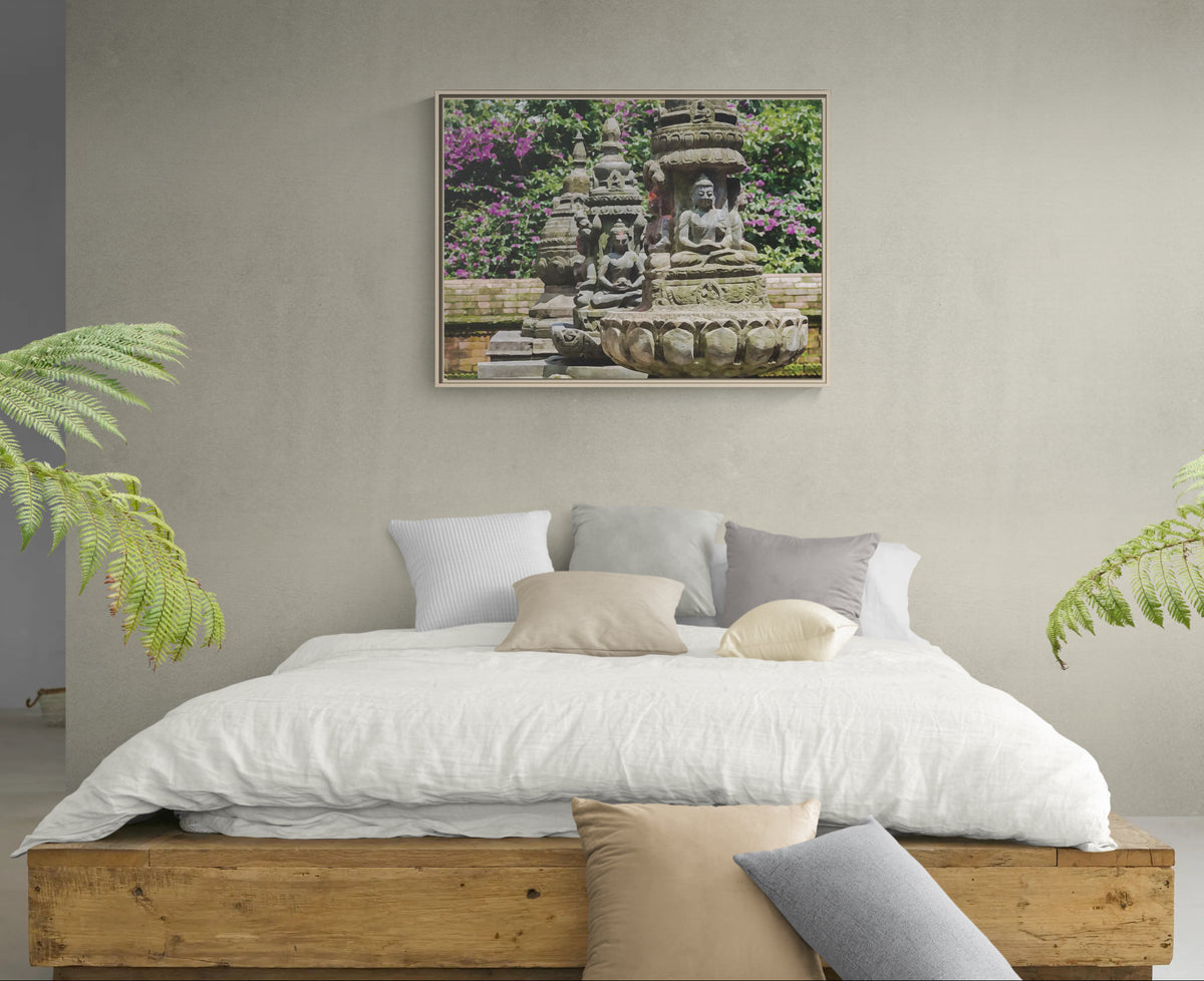 Framed wall art of stone Buddha statues in a garden above a wooden bed frame with white bedding