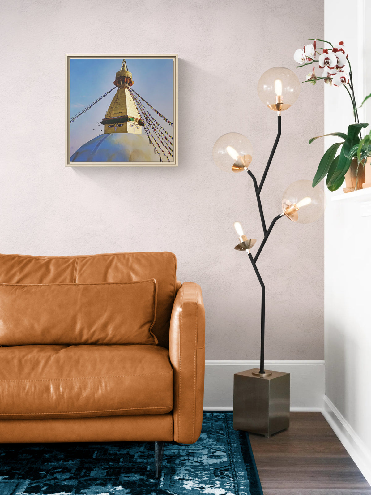 Framed print of Boudhanath Stupa hanging above a brown leather sofa next to a modern floor lamp