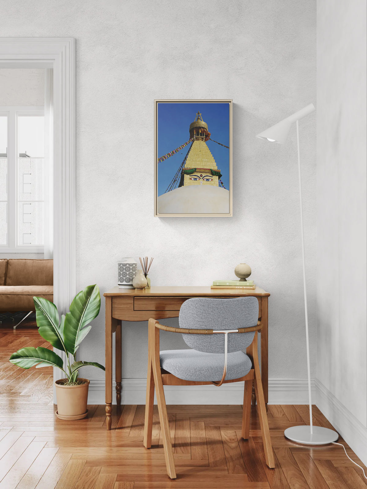 Framed print of Boudhanath Stupa hanging above a wooden desk with a chair and floor lamp