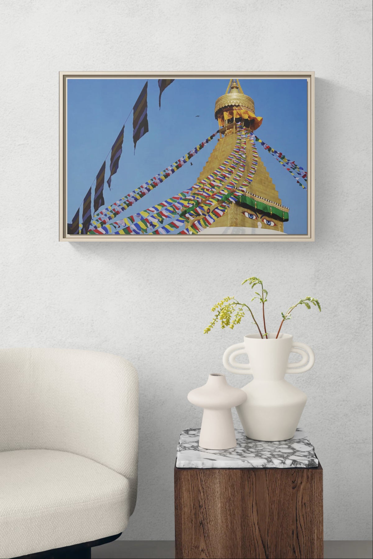 Framed wall art of Boudhanath Stupa with prayer flags hanging above a marble side table and white chair