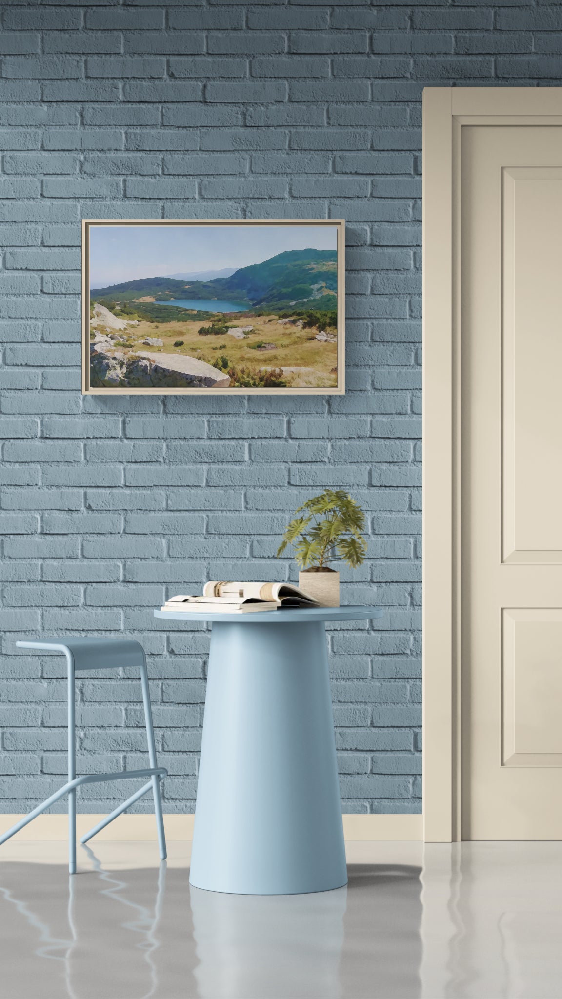 Framed landscape canvas of a mountain lake hanging on a blue brick wall above a small table and stool