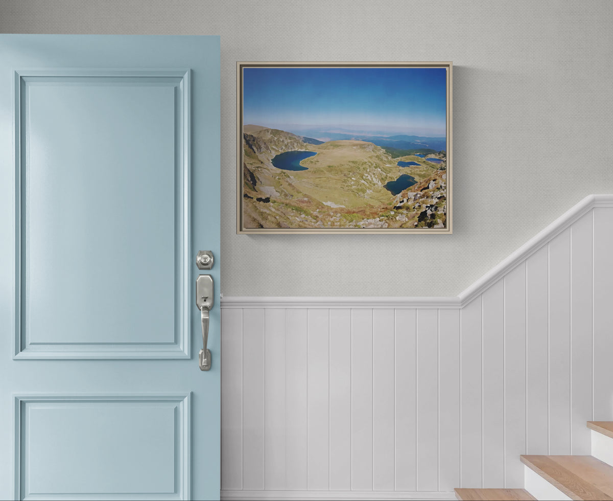 Framed landscape print of mountain lakes hanging on a wall next to a light blue door