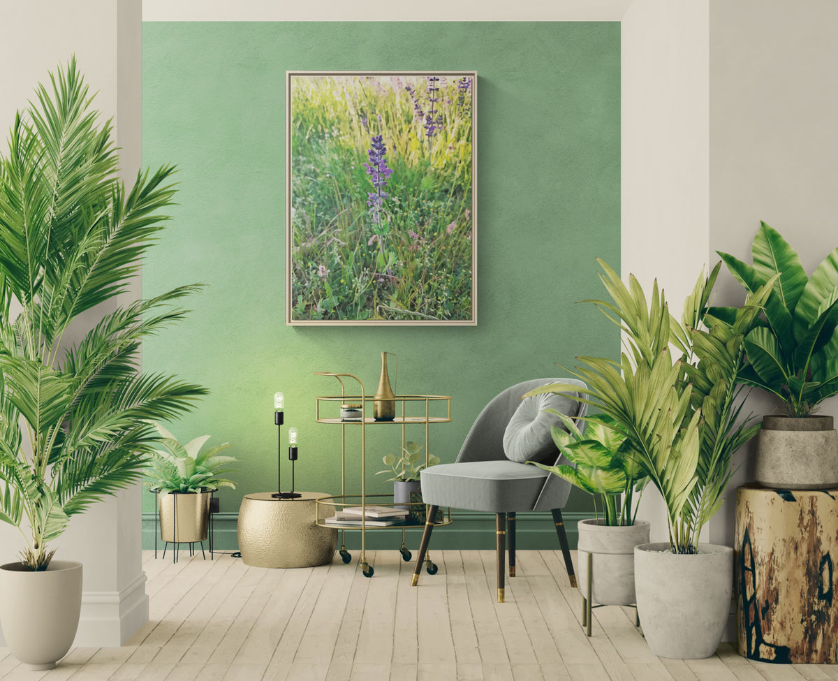 Framed floral wall art hanging on a green wall in a room with a grey chair and potted plants