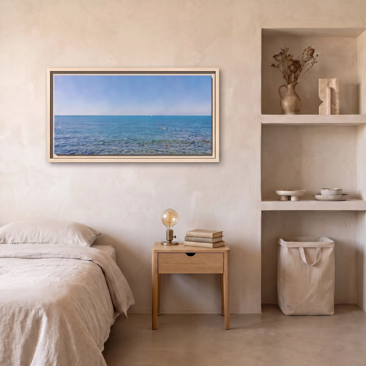 A framed horizontal landscape print of a blue sea under a clear sky, displayed on a textured beige wall in a minimalist bedroom setting with a bed, bedside table, and shelving.