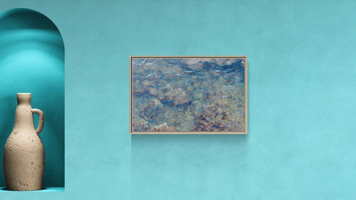 Framed wall art depicting clear shallow water over a rocky seabed on a blue wall with a decorative vase