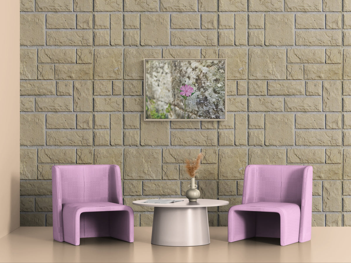 Two pink armchairs and a round table with a vase against a stone wall with a framed flower print