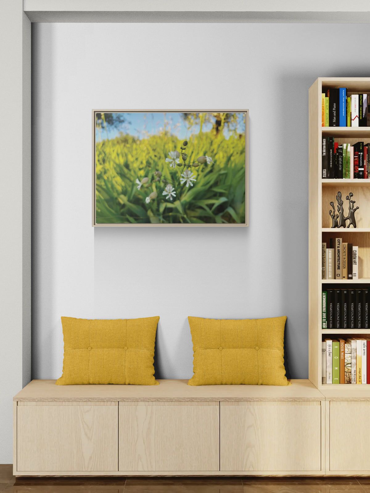 Framed wall art of white wildflowers in a green field above a wooden bench with yellow cushions
