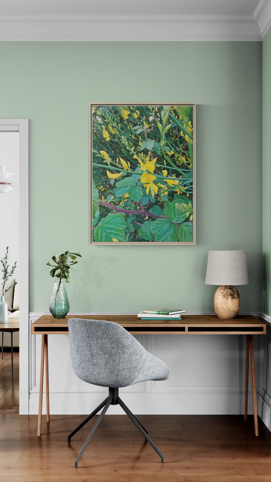 Framed botanical print of yellow flowers and green leaves hanging above a wooden desk with a grey chair