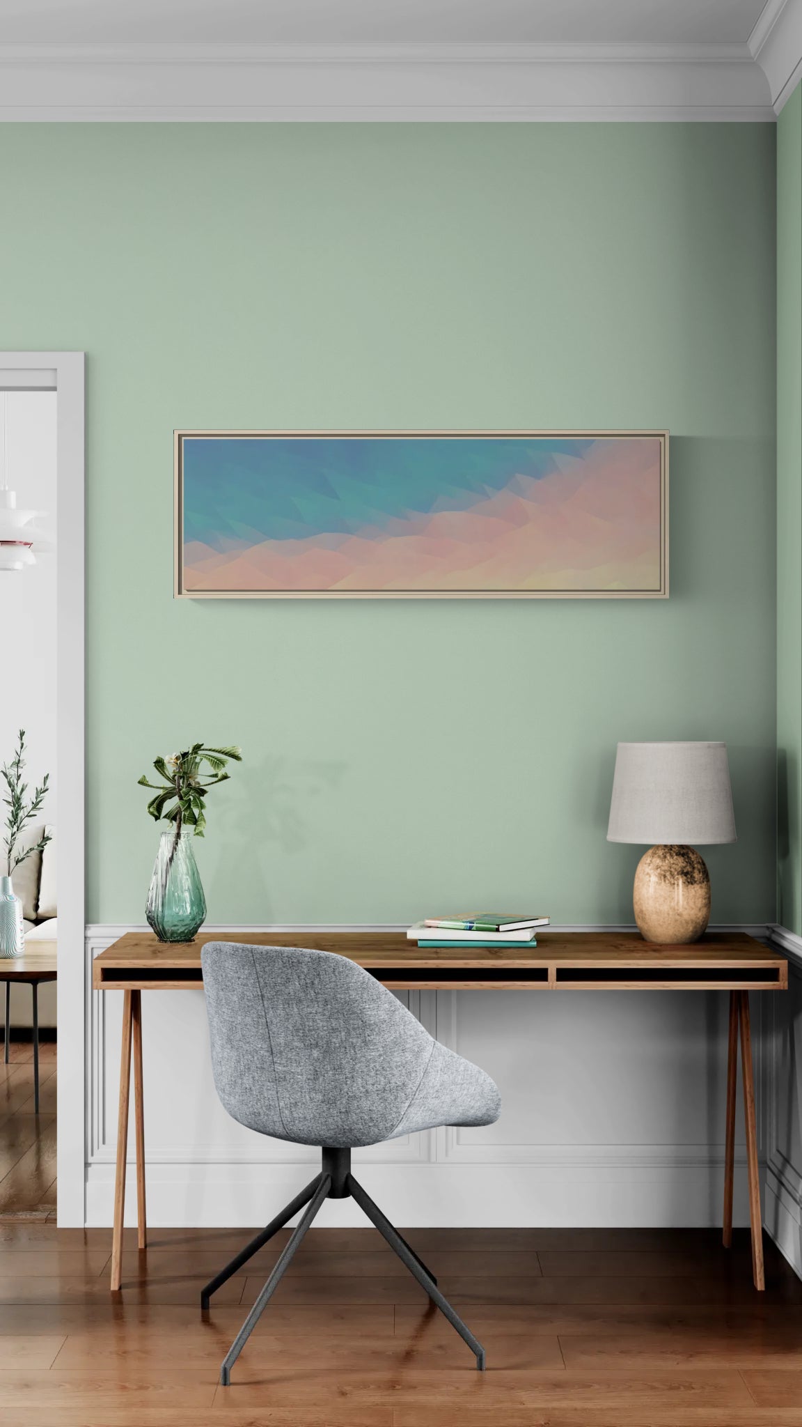 Panoramic abstract wall art in a wooden frame hanging above a wooden desk with a grey chair and lamp