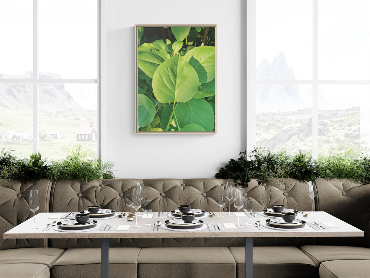 Framed wall art of green leaves hanging above a dining table with place settings