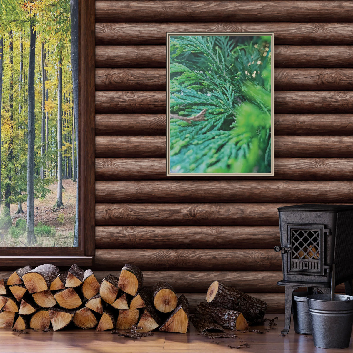 A framed vertical art print depicting vibrant green pine needles, styled on a rustic brown log wall above a wood-burning stove and a stack of firewood.