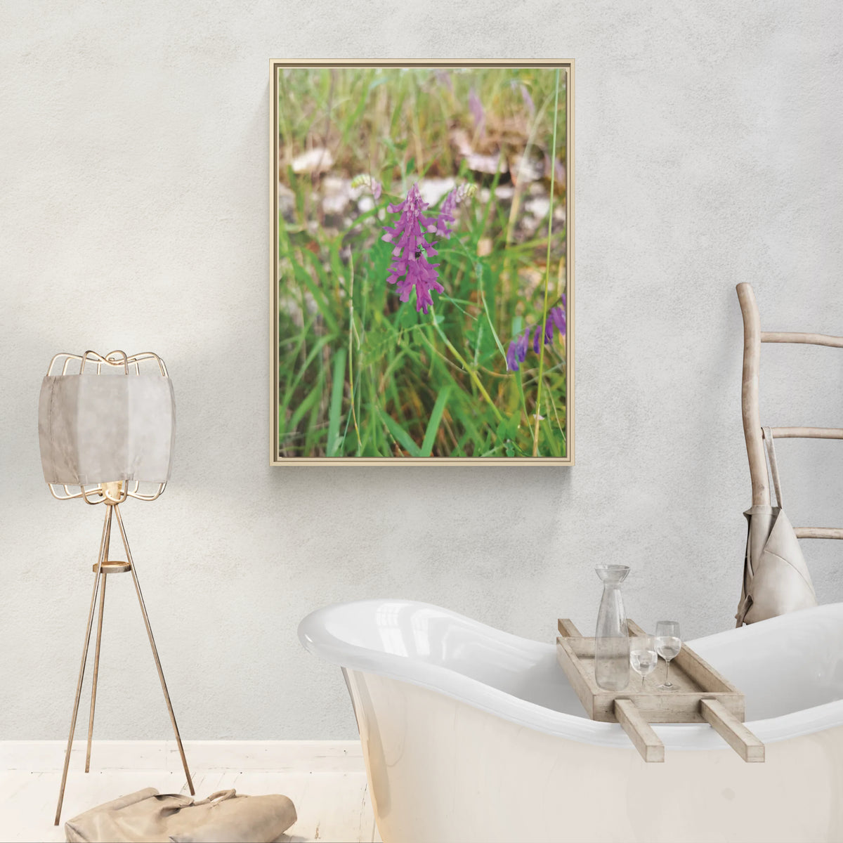 Framed wall art of purple wildflowers in a bathroom with a freestanding tub and tripod lamp