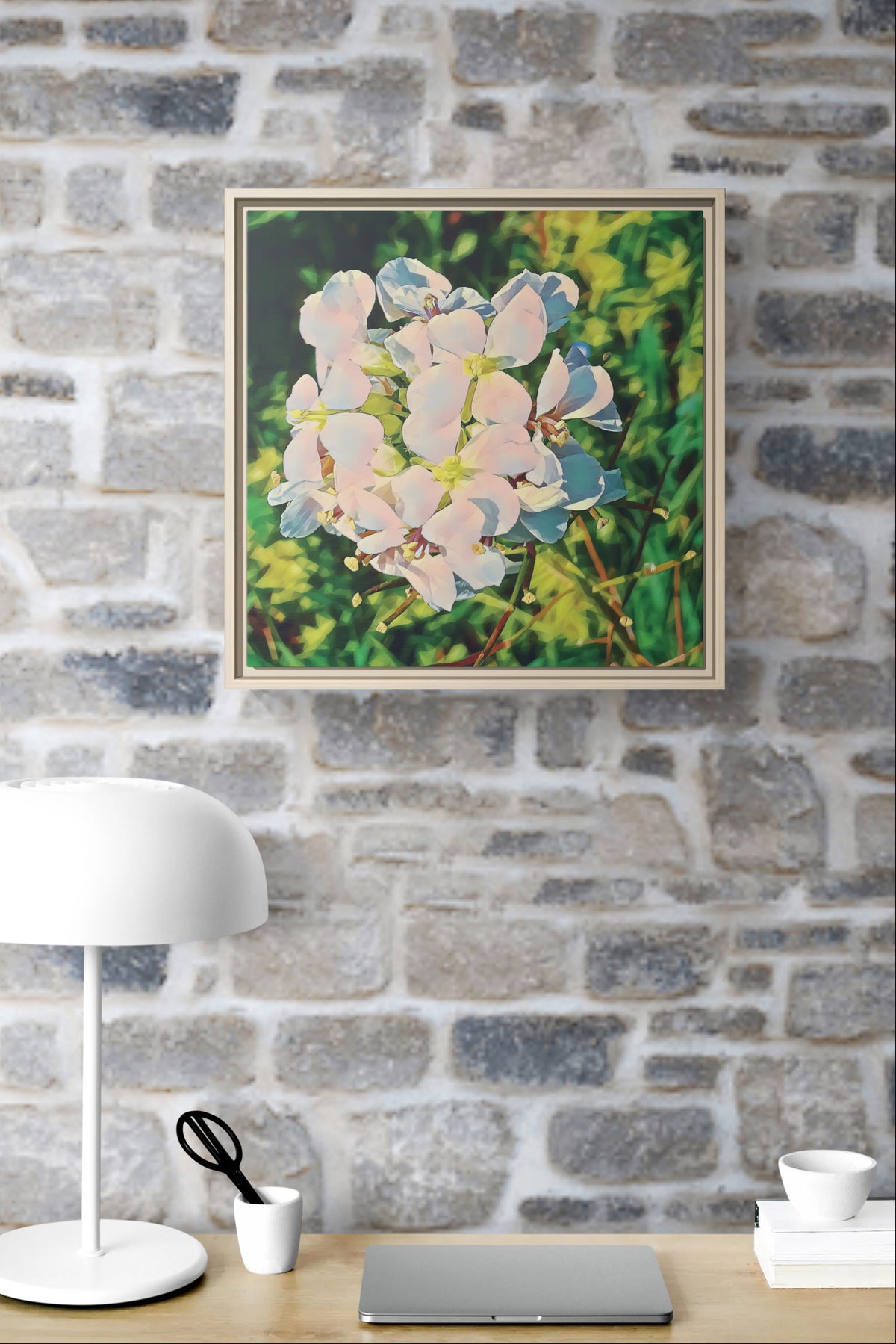 Framed floral canvas hanging on a stone wall above a desk with a lamp and laptop